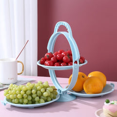 Image du Plateau à Fruits Pliable à Double Étage Quebekado, montrant ses deux niveaux en configuration dépliée. Disponible en couleurs rose, bleu et vert, ce plateau en ABS de haute qualité est affiché dans un intérieur moderne, mettant en valeur son design élégant et fonctionnel