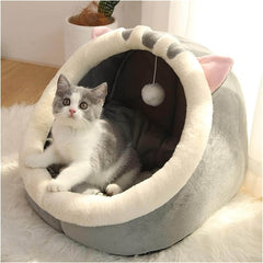 Maison Douillette pour Chat Quebekado, présentant un lit-tente confortable en flanelle douce avec une entrée triangulaire et des oreilles de lapin design. L'intérieur montre un coussin moelleux amovible, idéal pour le repos des chats. La tente est placée sur un sol lisse, illustrant sa base antidérapante et sa stabilité.